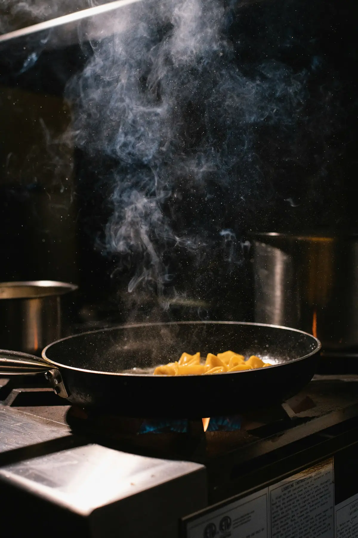 Pfanne auf offener Gasflamme, Dampf steigt in der dunklen Küche auf