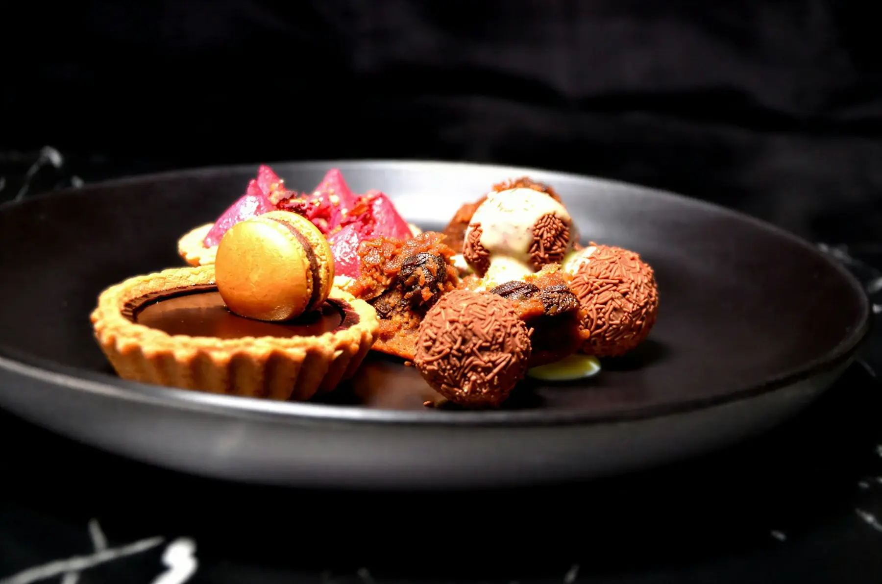 Pralinen, Tarte und kleines Gebäck auf einem dunklen Teller