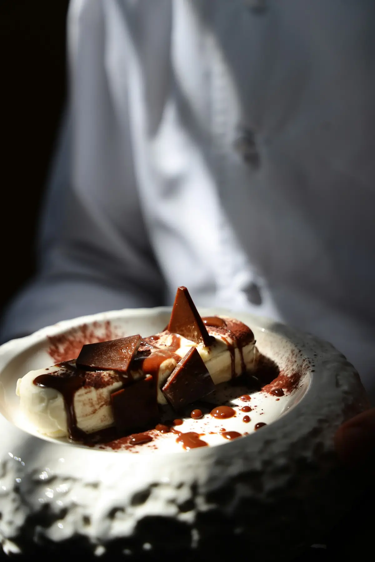 Dessert aus dunkler Schokolade mit Kakaostaub in einer hellen Steinschale