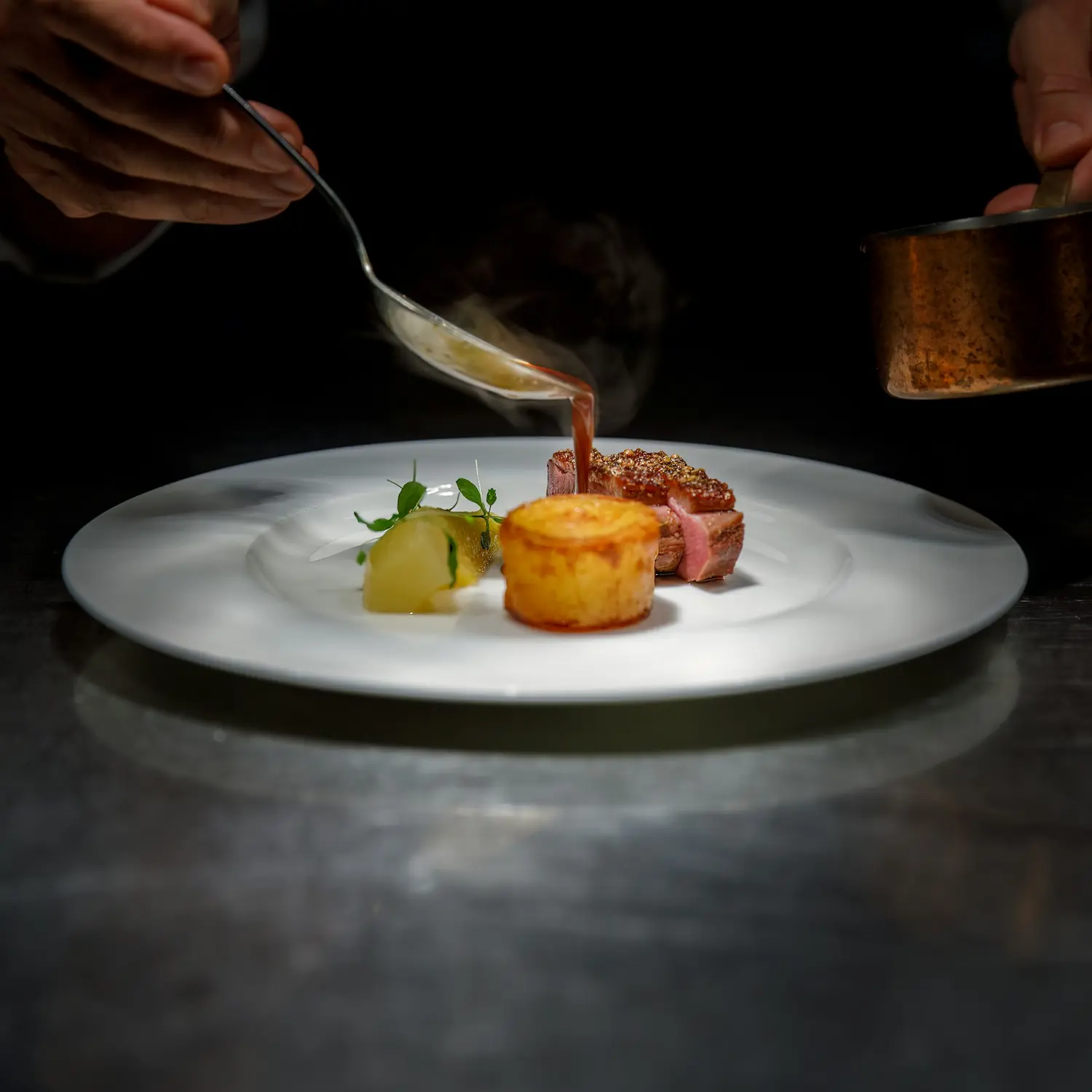 Koch gießt mit dem Löffel Jus über ein Stück Rind mit Kartoffelfondant