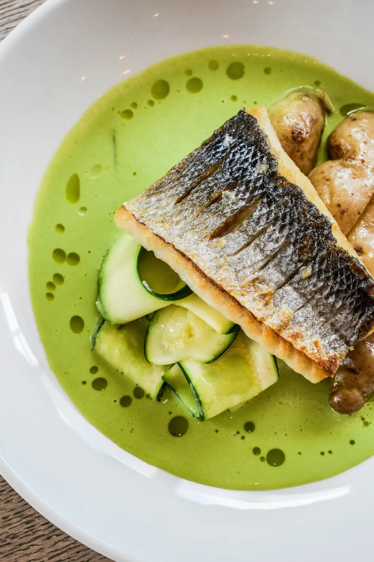 Wolfsbarsch auf der Haut gebraten, mit Zucchini und Kartoffeln in grünem Kräutersud